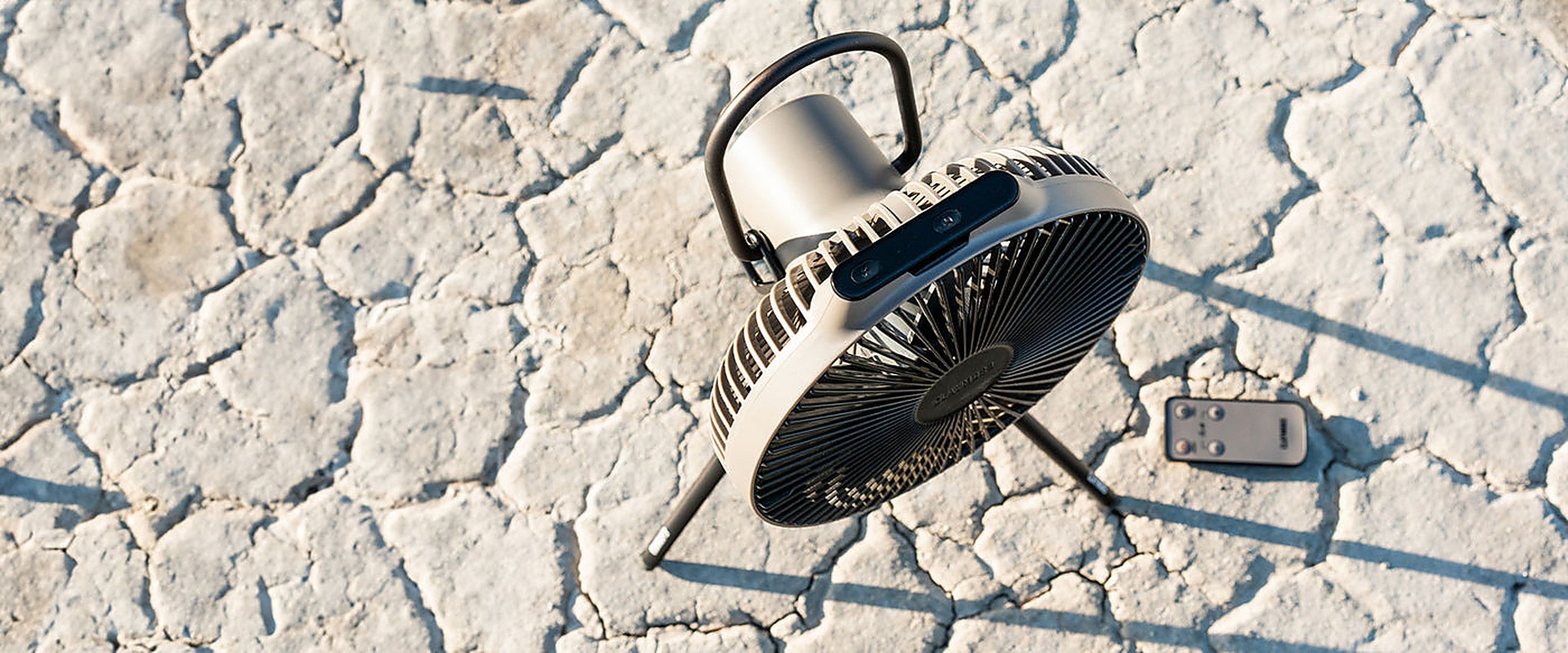 Warm Grey V1040 fan with its remote set on desert ground at a campsite
