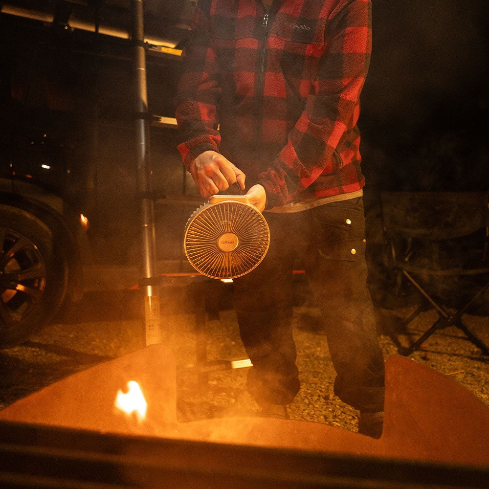 Person carrying the V600+ fan by its handle at night near a fire pit