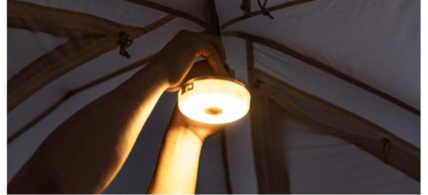 Hand holding the lit lantern up inside a tent