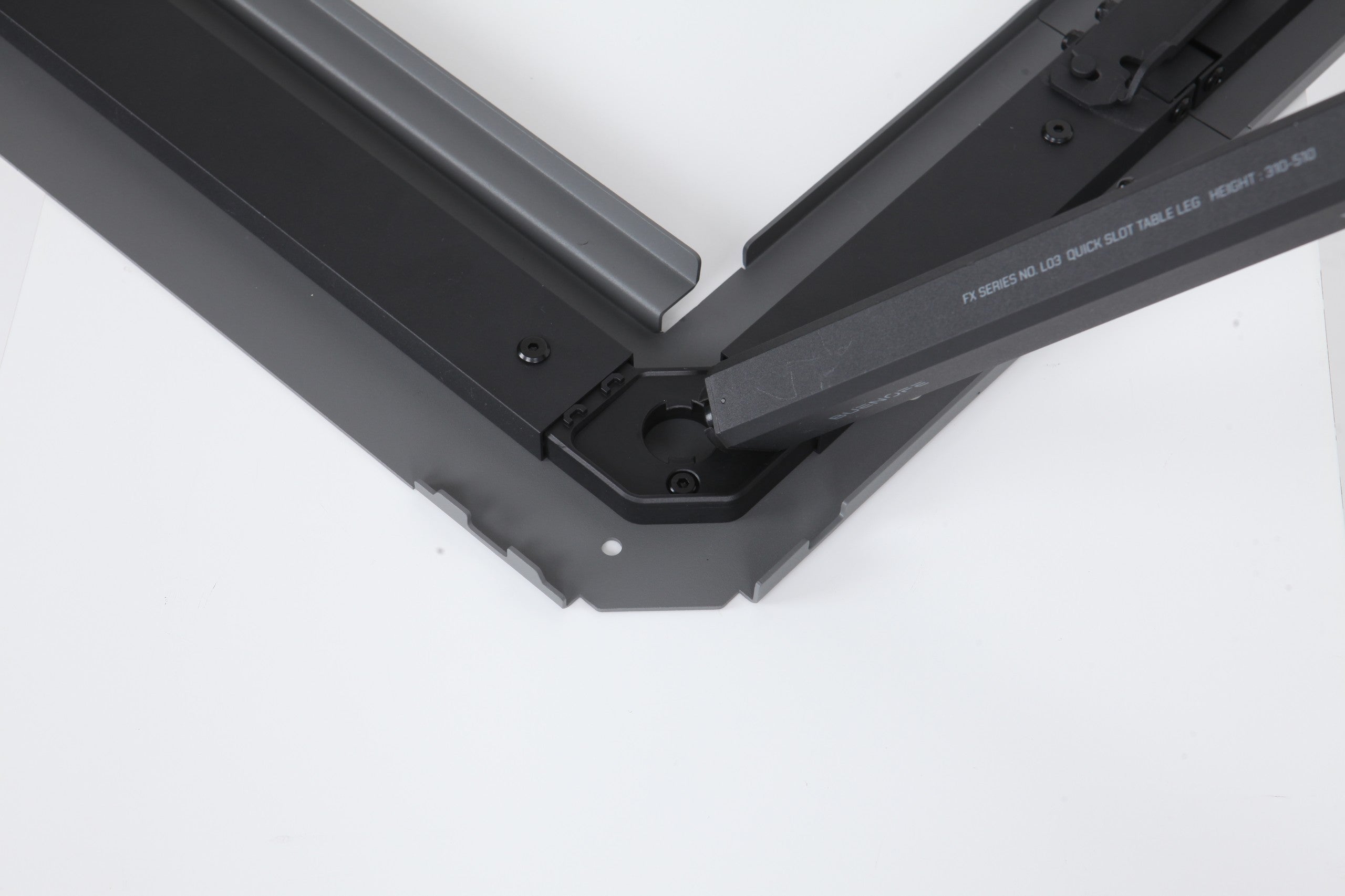 BUENOFE IGT Quick Slot Table Leg shown being inserted at an angle into the corner slot of a black IGT frame on a white background, demonstrating how the engraved leg drops into the frame groove before twisting to lock.