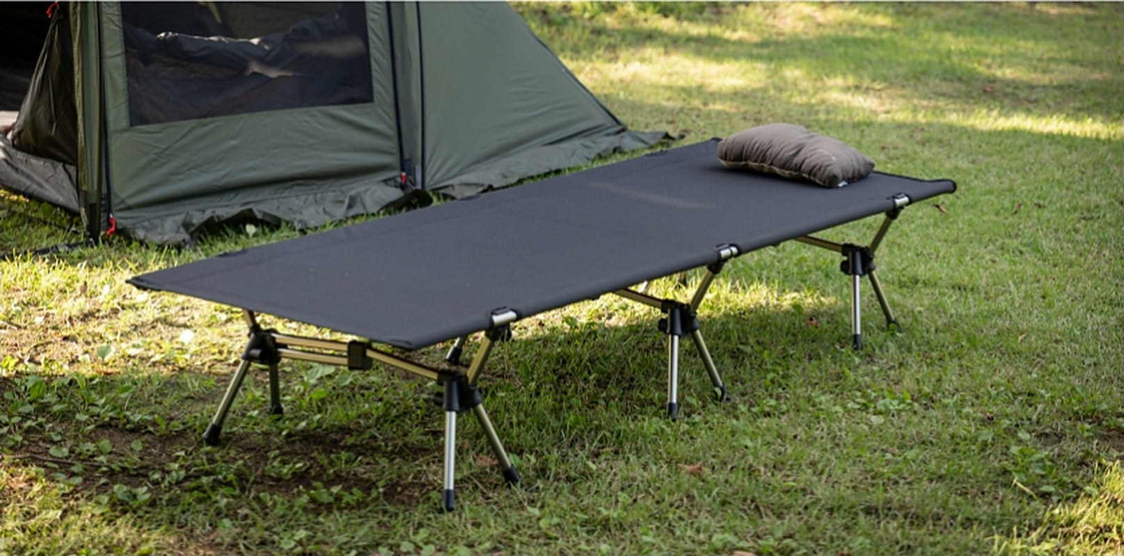 Camp cot set up in front of a tent with a pillow, ready to use