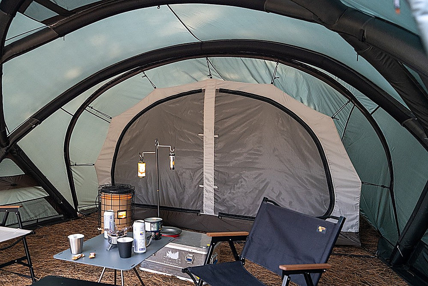 Wide view of Shelter GM living area with the Vestibule Inner Tent at the rear, camp table, chair and hanging lanterns