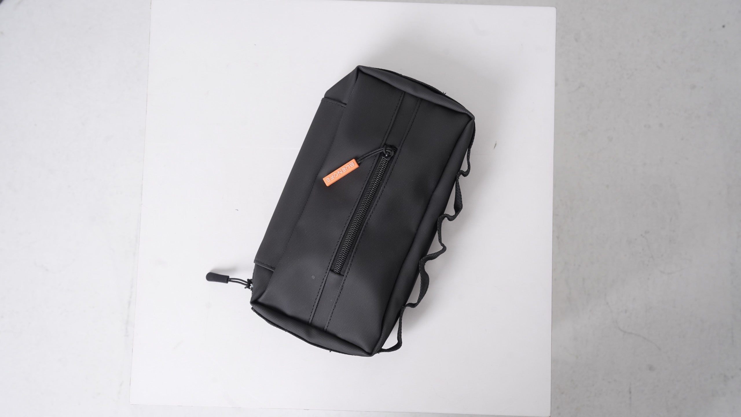 BUENOFE Multi Storage Bag Slim detachable tissue pouch shown on its own on a white board, a compact black zippered pouch with an orange BUENOFE zipper pull and side elastic loops.