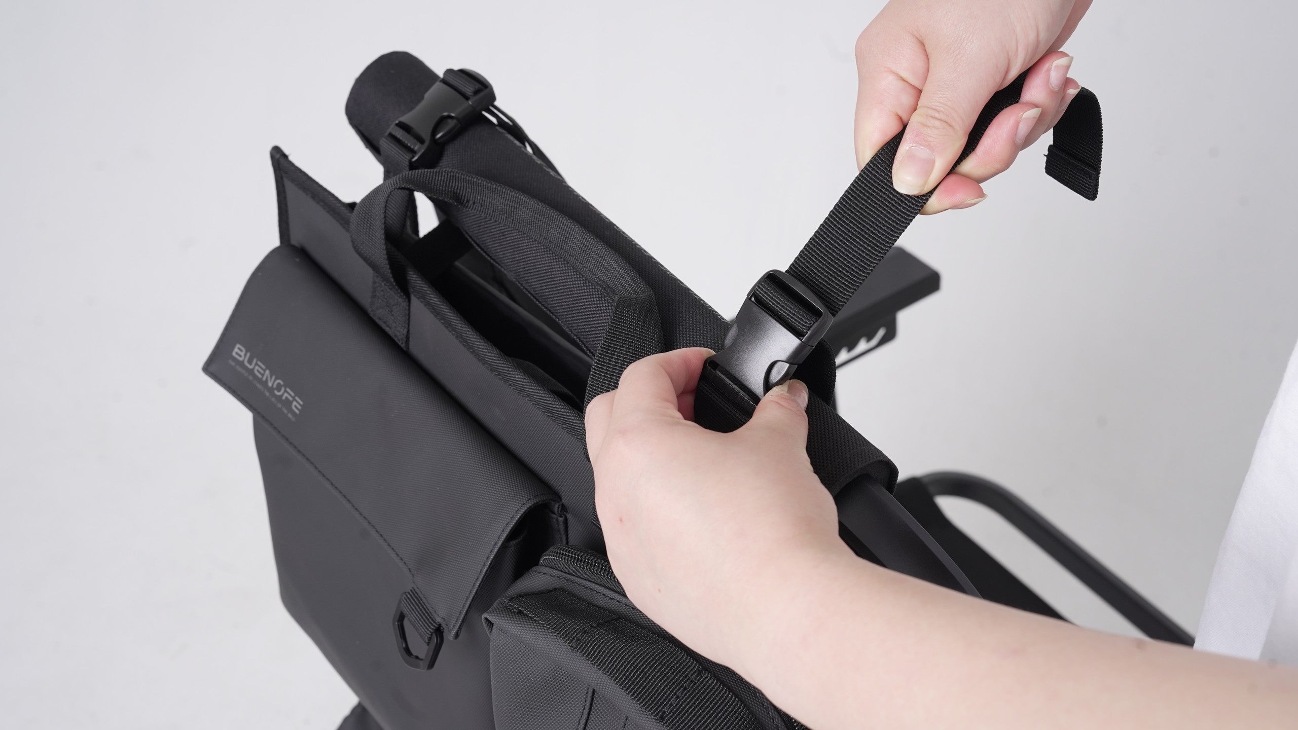 BUENOFE Multi Storage Bag Slim being mounted on a camp chair as hands loop the top strap over the chair frame and connect the side-release buckle, illustrating the quick chair-mount step.