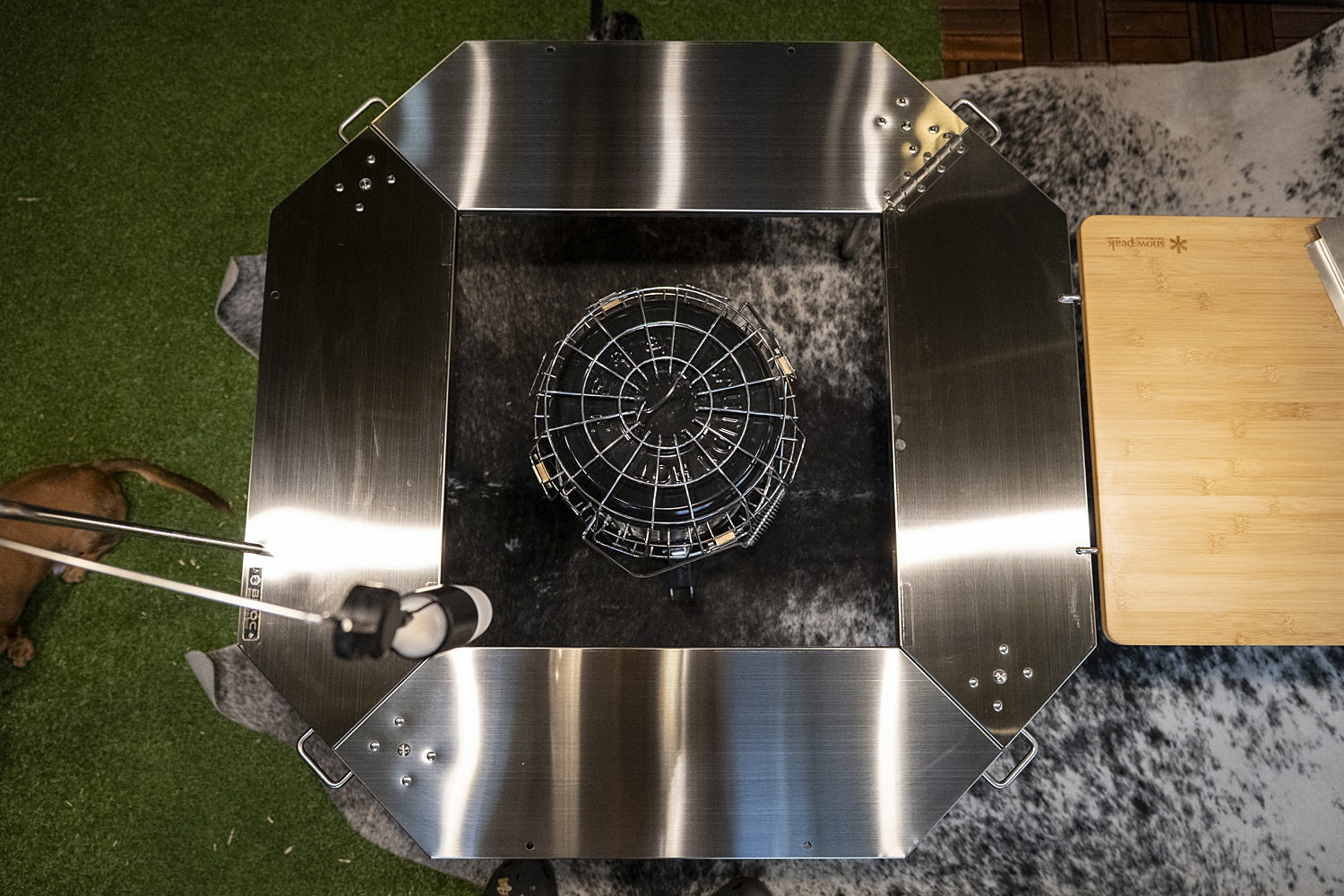 Octa table from above with the centre open and a stove standing on the ground inside the ring, set up beside a side table. The stove, lantern and side table shown are not included.