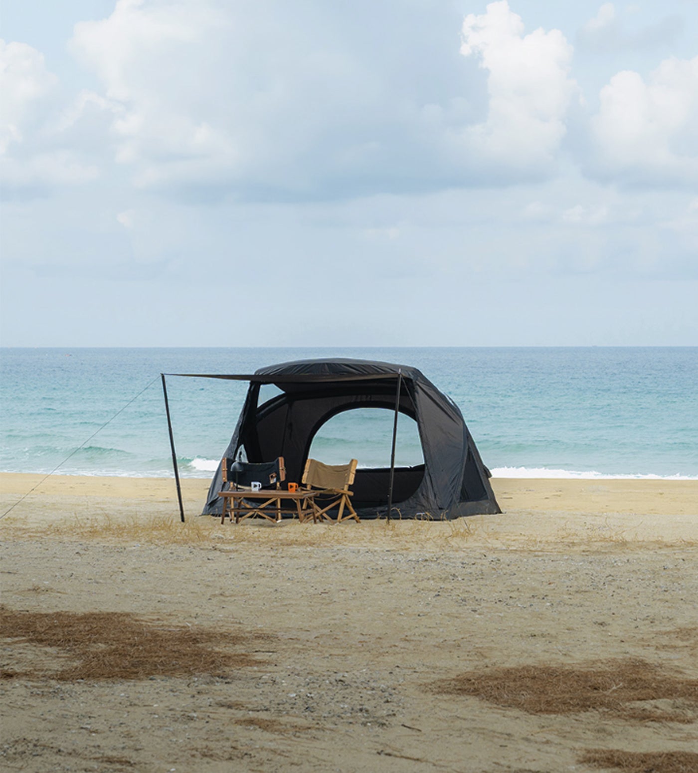 theEarth GEO AIR4 Tent, Black, open front on a beach with camp chairs and ocean view