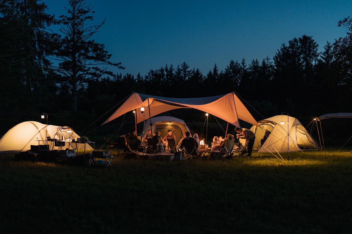 People gather under Snow Peak's Tarp with lights on in the night.