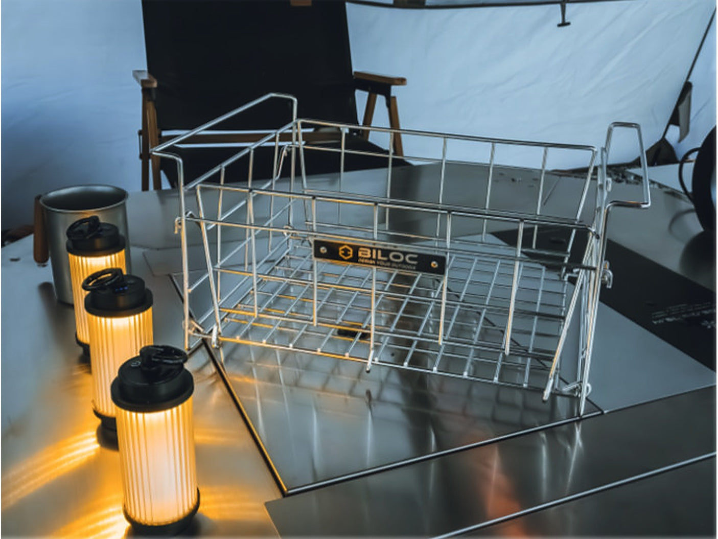 Folding wire basket in use on a camp table, beside lanterns.