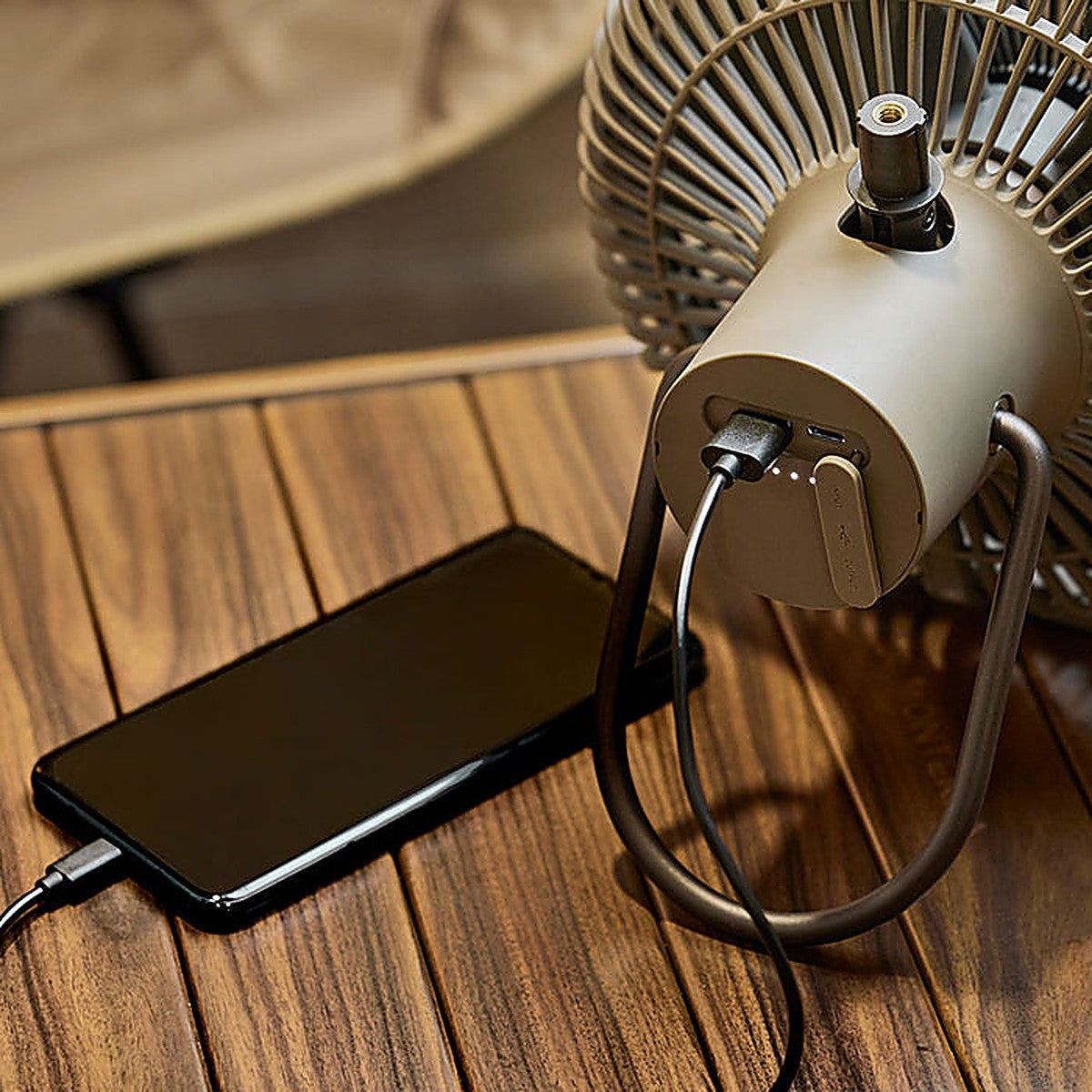 Smartphone charging from the USB-A output port of the V1040 fan at a campsite