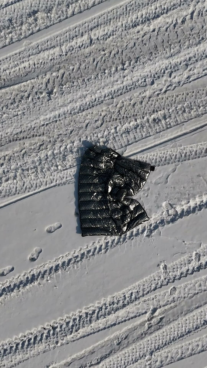 Black DEOS camp comforter on open snow, aerial