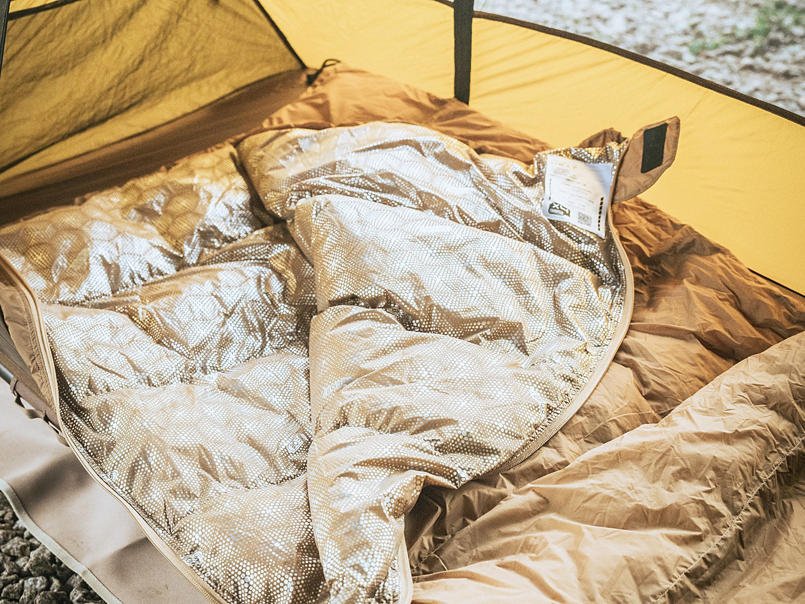 Tan DEOS camp comforter opened in a tent showing the heat-reflective lining