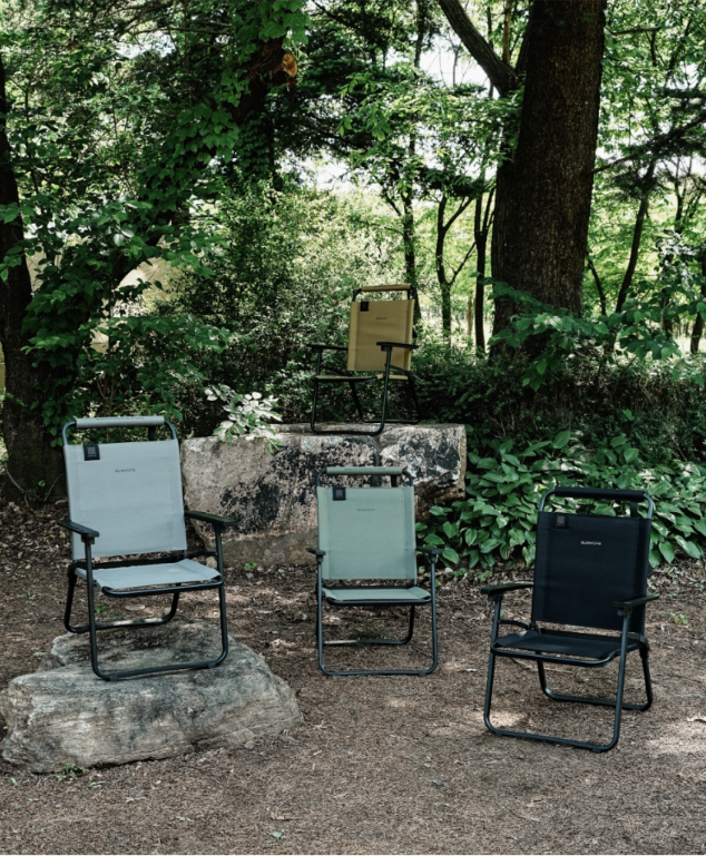 Four BUENOFE FLOW folding chairs in gray, khaki, black, and tan set up together at a forest campsite