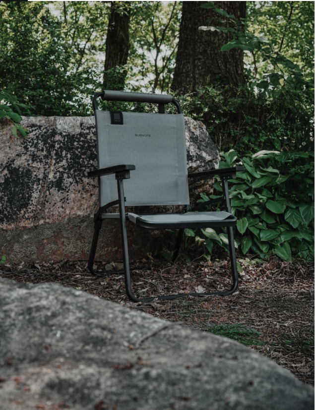 Gray FLOW folding chair set up outdoors among rocks and forest greenery