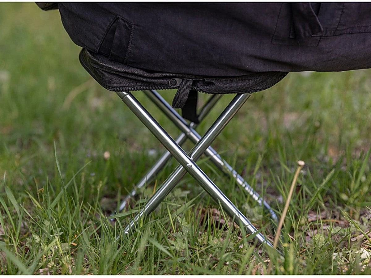 Person sitting on the folding stool, the cross-leg frame supporting their weight on grass