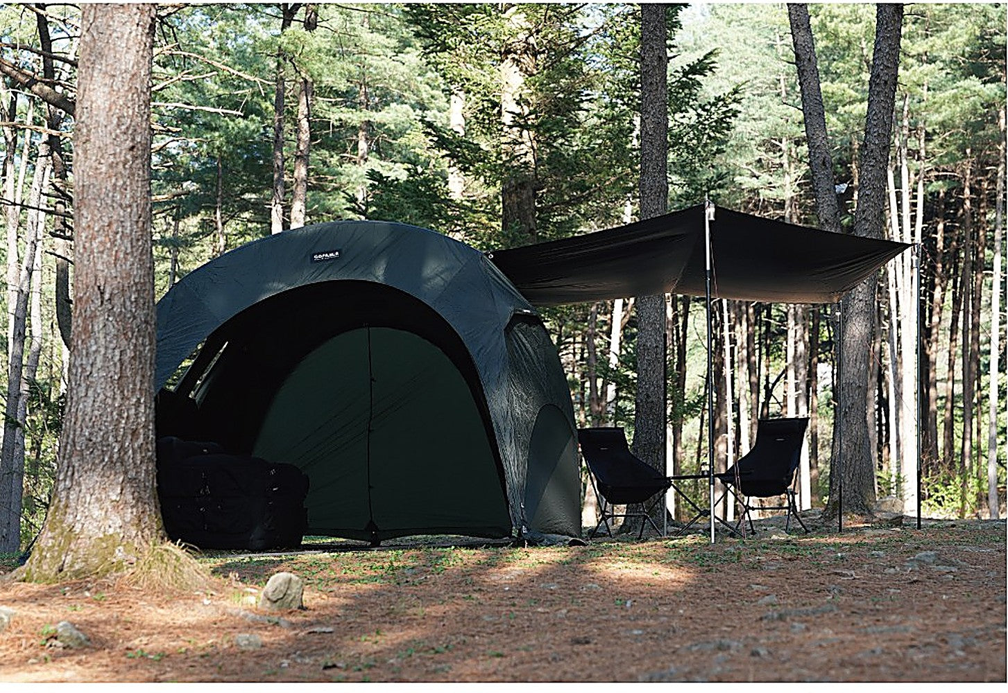 Side view of the T720+ Side Tarp stretched from the black dome tent over two camp chairs in the woods