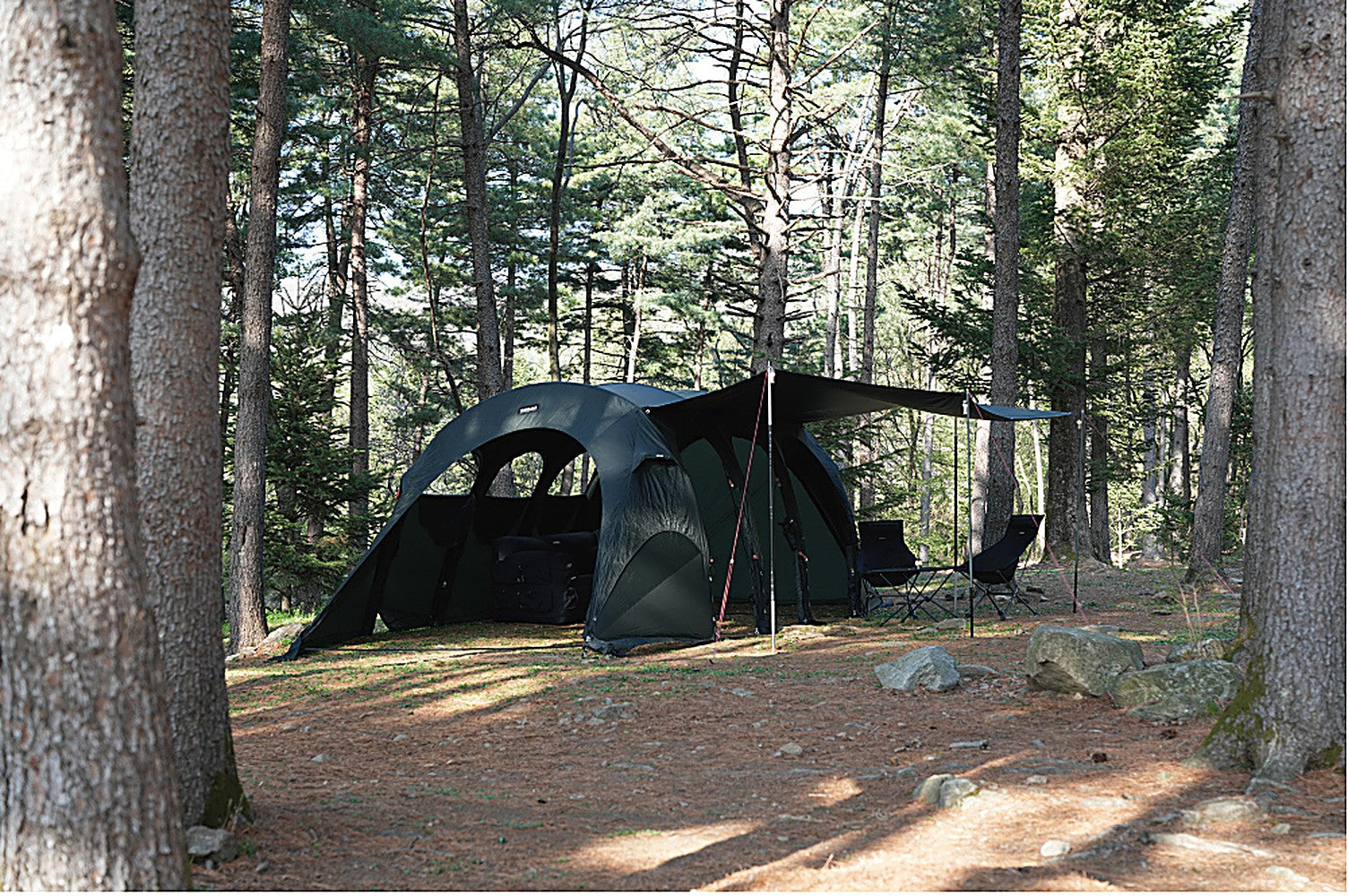 Side tarp extended off the Gopamir T720+ shelter creating a covered open-air seating area with chairs in a forest