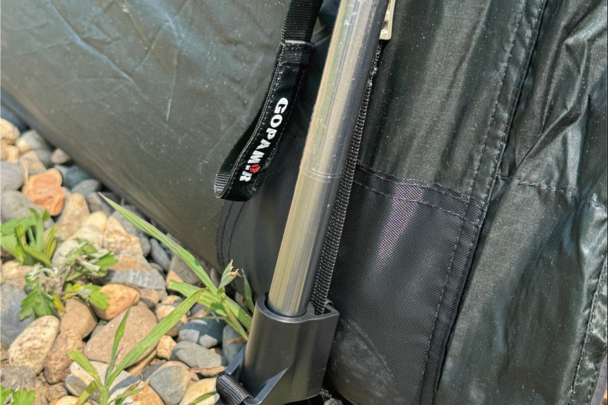 Pole in carry bag alongside camping gear for scale