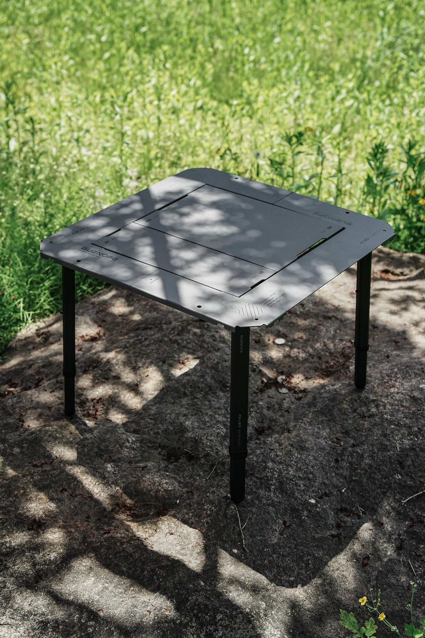 BUENOFE IGT Connect Table 1.5 built into a graphite-gray standalone table on a flat rock in a sunlit meadow, dappled light falling across the surface.