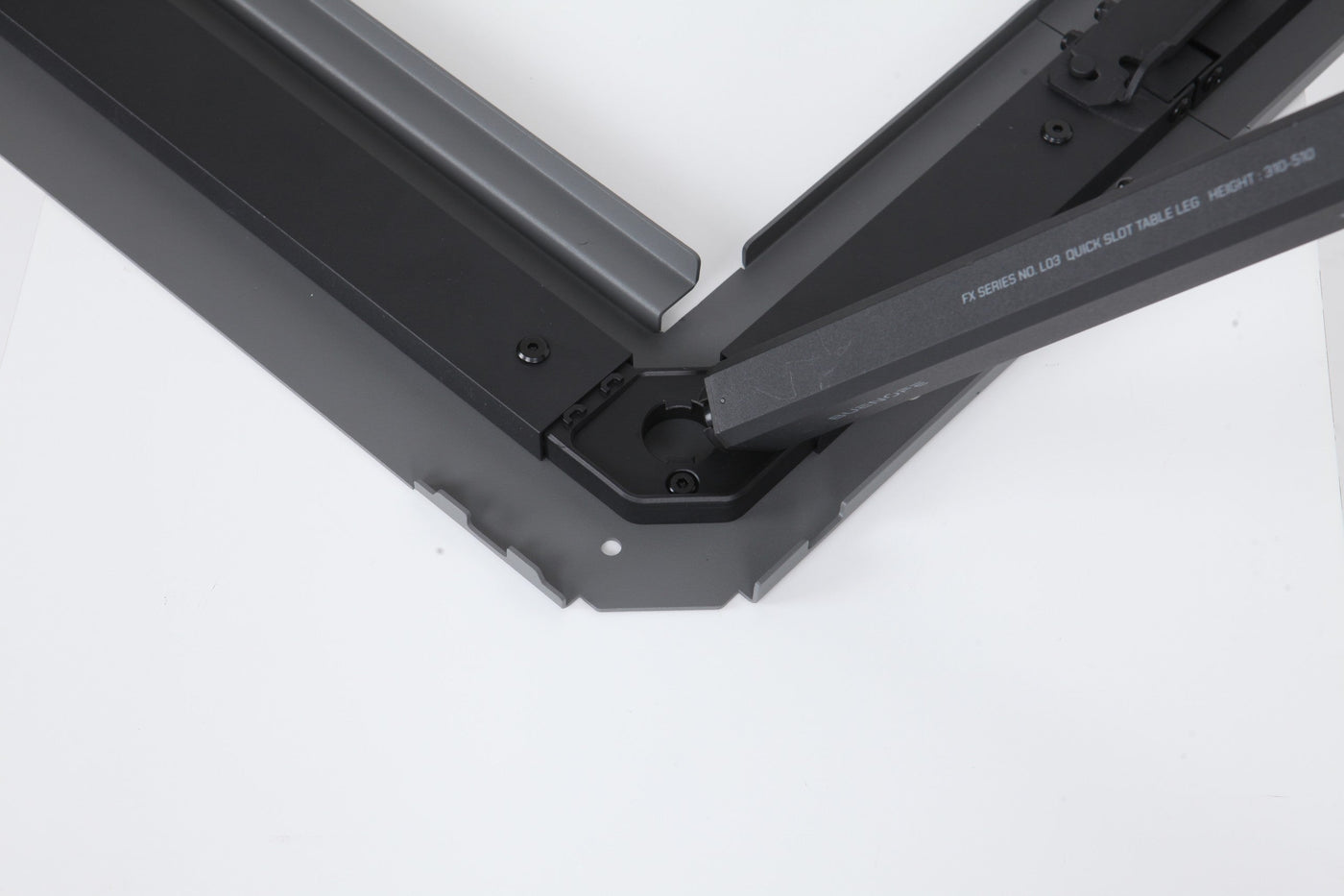 BUENOFE IGT Quick Slot Table Leg shown being inserted at an angle into the corner slot of a black IGT frame on a white background, demonstrating how the engraved leg drops into the frame groove before twisting to lock.