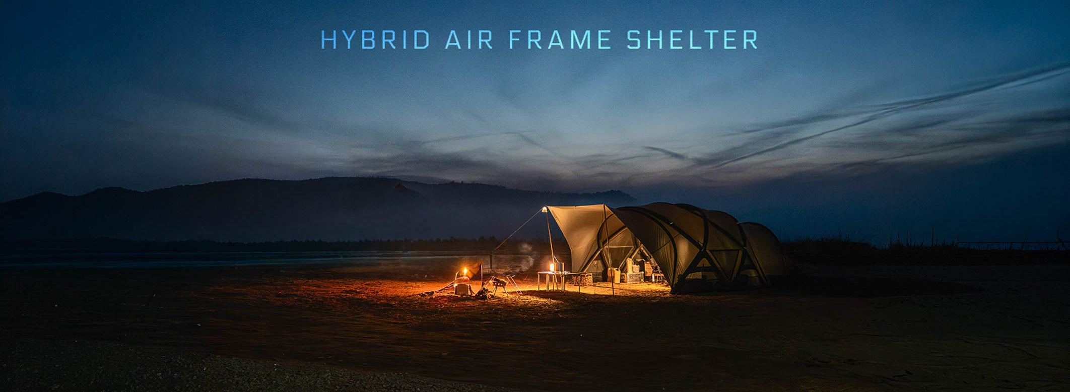 Minimal Works Shelter GM hybrid air-frame dome shelter with awning lit at a campsite at dusk