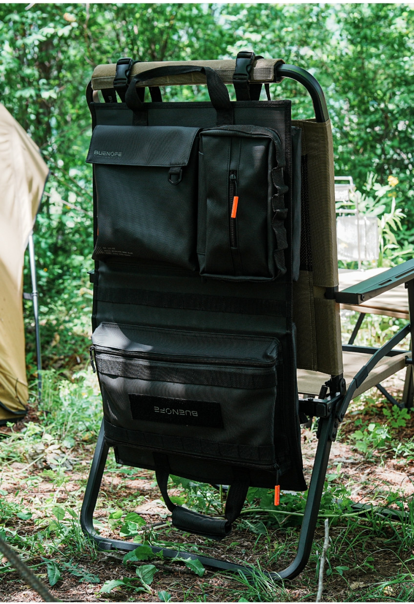 BUENOFE Multi Storage Bag Slim mounted upright on the back of a camp chair at a forest campsite, its flap pocket, tissue pouch and lower zip pocket filled and within easy reach beside a tent and a camp table.