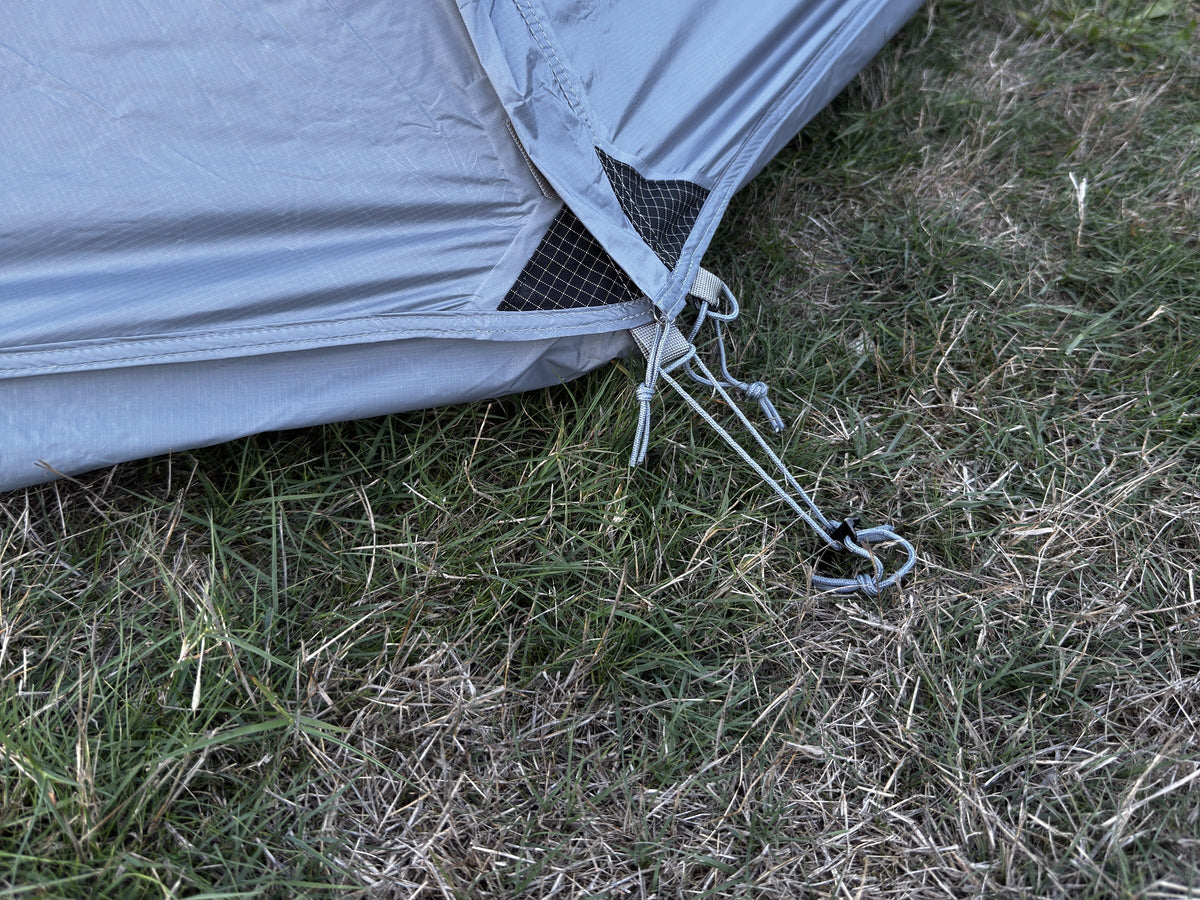 Corner of the Air rainfly pegged to the ground with its guy line.