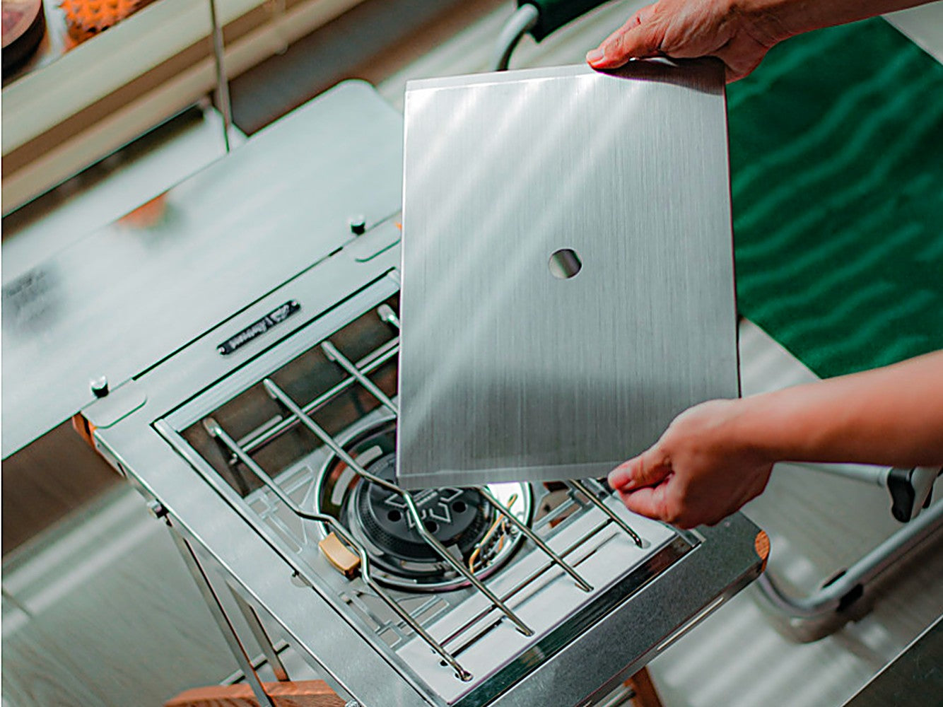 Hand lowering the stainless Flat Cover onto the Personal Flat Burner in a table setup