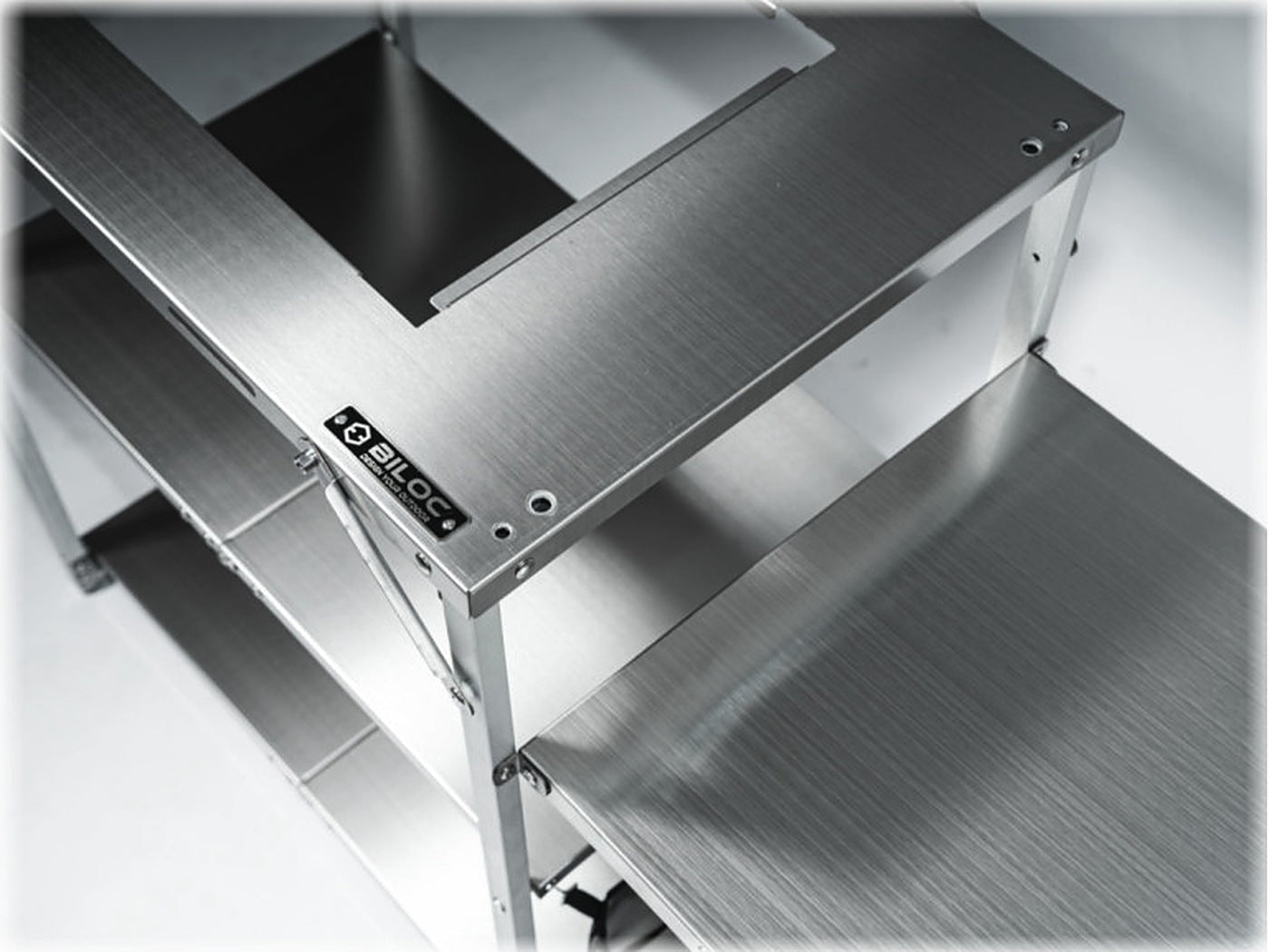 Close-up of the BILOC nameplate on the stainless top plate, with the aluminium frame and shelf tier below.