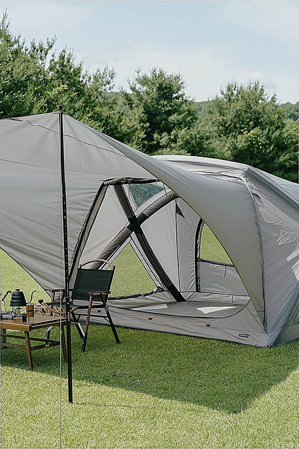 Close-up beneath the GEO AIR4 Extension Sun Shade: black pole, camp chair and coffee table by the tent's mesh door